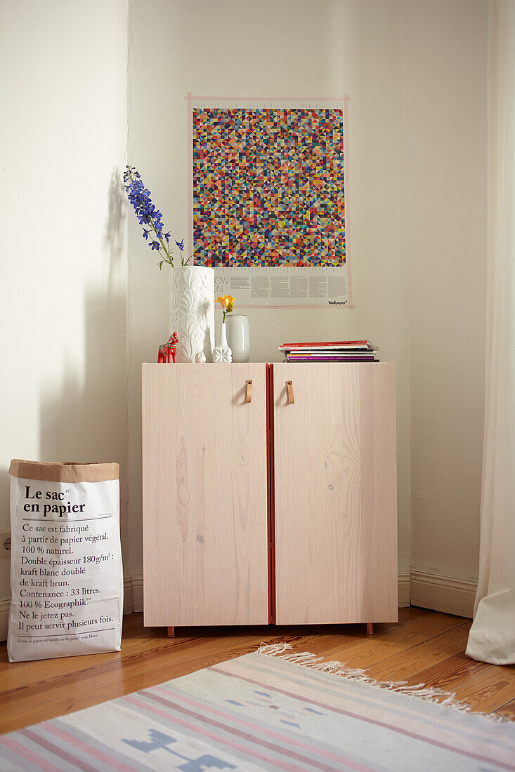 Wooden cabinet with vases and magazines, colorful picture on white wall