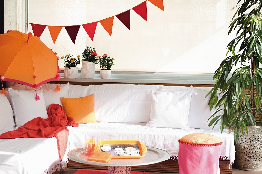 Gemütliche Sitzecke mit weißem Bezug, orangefarbener, balinesischer Sonnenschirm und Wimpelgirlande
