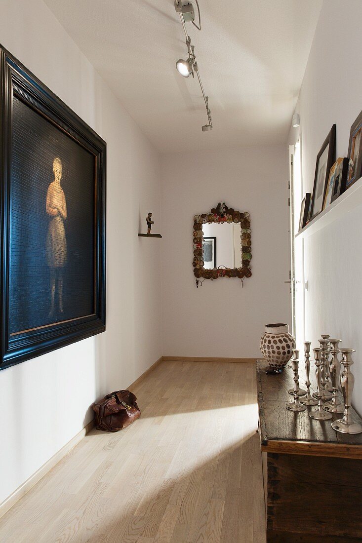 Narrow corridor with traditional ambiance; oil portrait in black frame and collection of silver candlesticks on antique cabinet