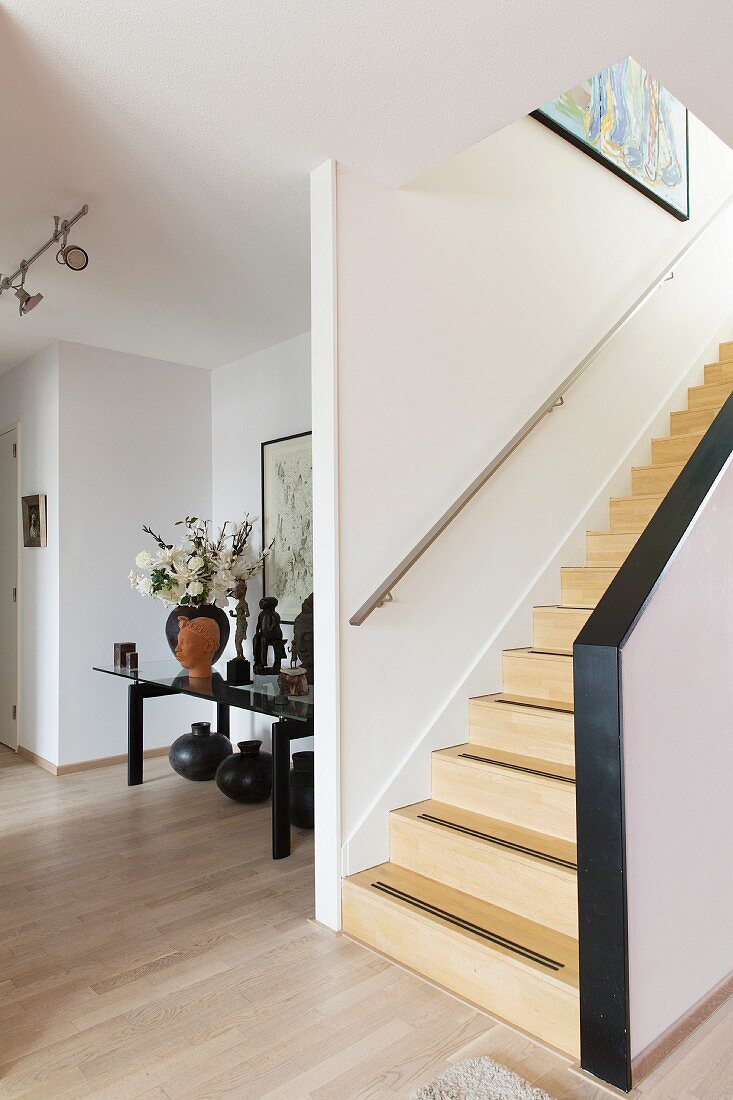 Treppenaufgang mit Holzstufen, seitlich Glastisch mit Kunstobjekten in Nische in offenem Wohnraum