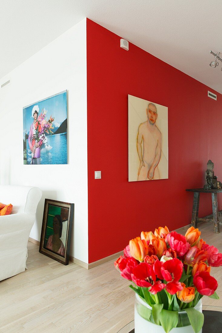 Red and orange tulips in front of male nude artwork on red-painted accent wall in modern interior