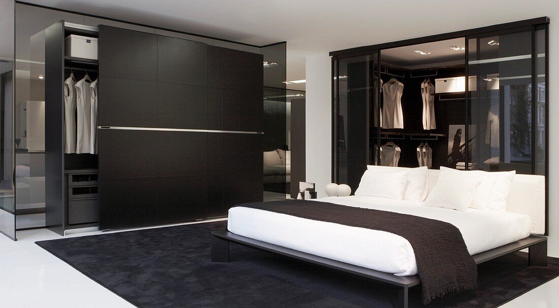 Schlafzimmer in Schwarz und Weiß, Doppelbett neben Kleiderschrank mit geöffneter Schiebetür in Schwarz