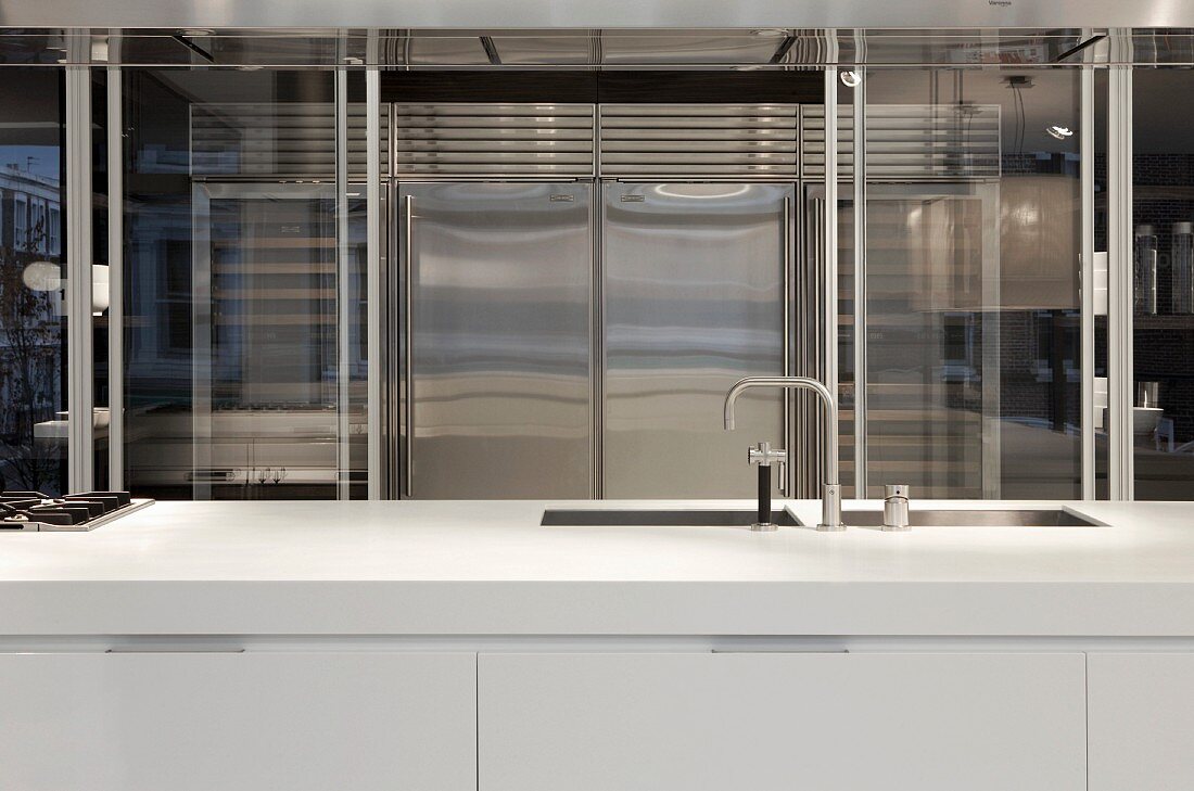 weiße Designer-Küchentheke mit Spülbecken vor Edelstahl Kühlschrankkombination