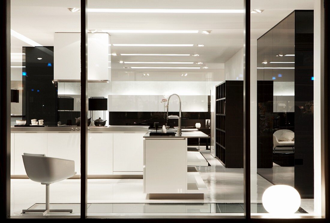 View through shop window of designer kitchen in showroom; white swivel chair and white counter in open-plan kitchen area