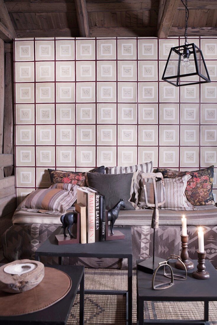 Beistelltische aus Metall mit Kerzen und Büchern, gemütliche Sitzbank mit Kissen vor Wand mit Vintage Tapete