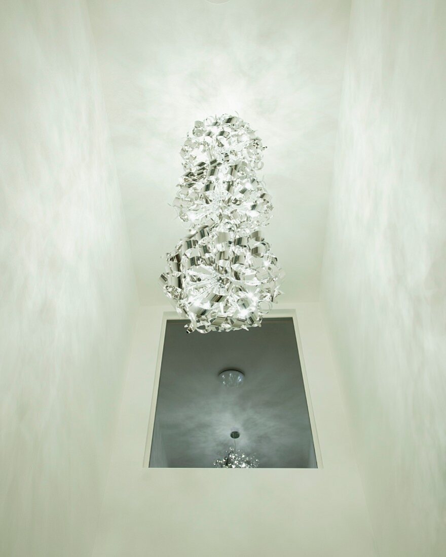 Pendelleuchte mit mehreren kugelförmigen Schirmen übereinander an Decke, im Hintergrund an Wand aufgehängter Spiegel