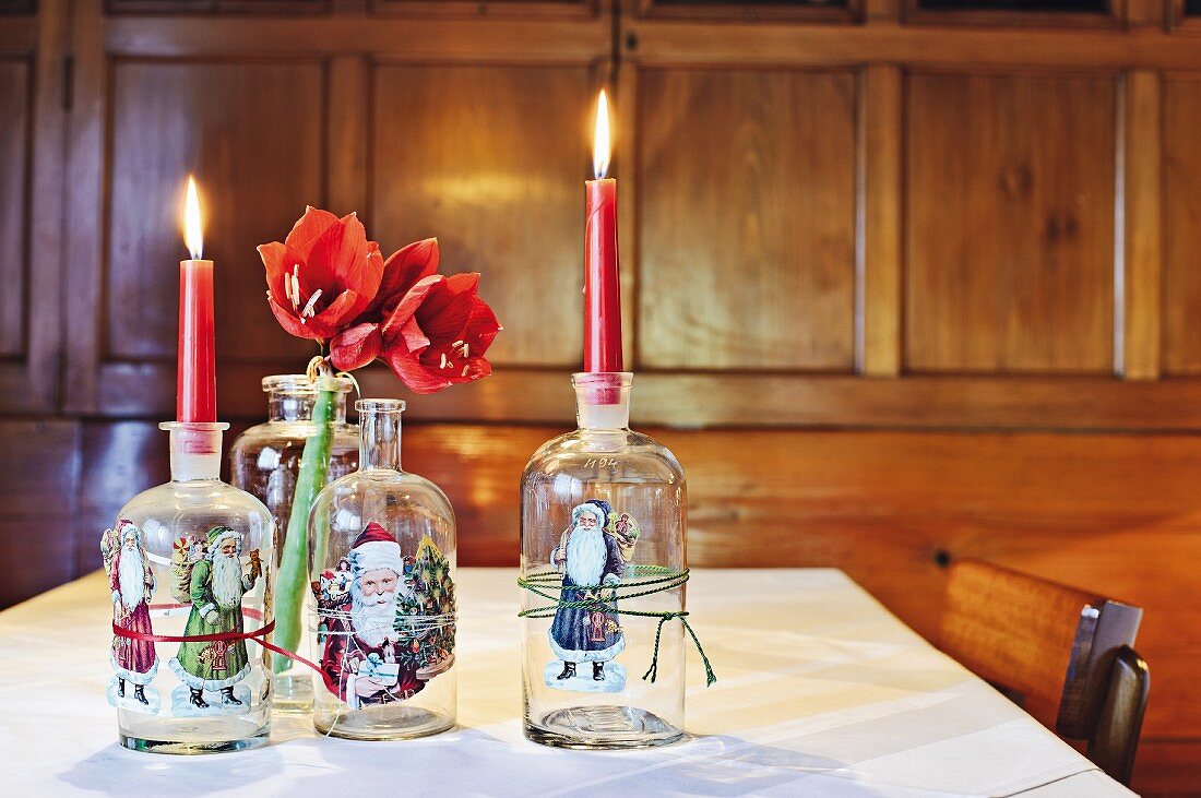 Alte Glasflaschen, mit Weihnachtsmotiven beklebt, als Kerzenhalter