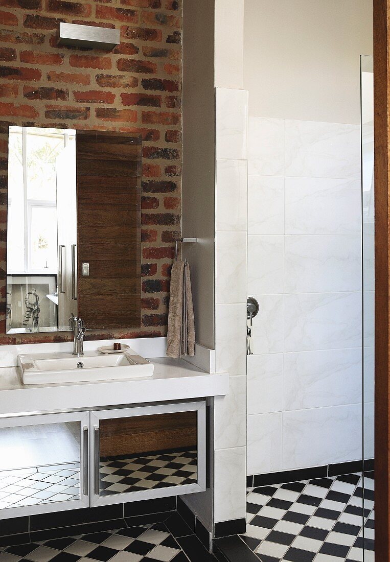 Washstand and mirrored cabinet on exposed brick wall and chequered floor in bathroom