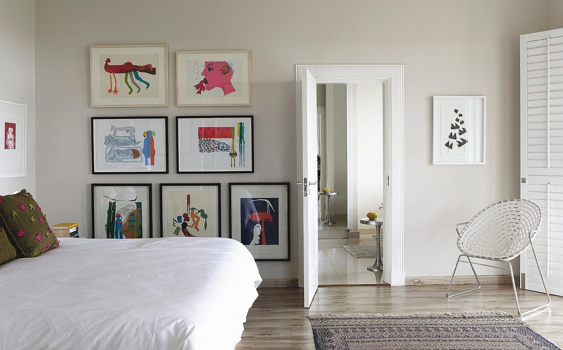 Double bed with white bedspread and gallery of artworks on wall in modern bedroom