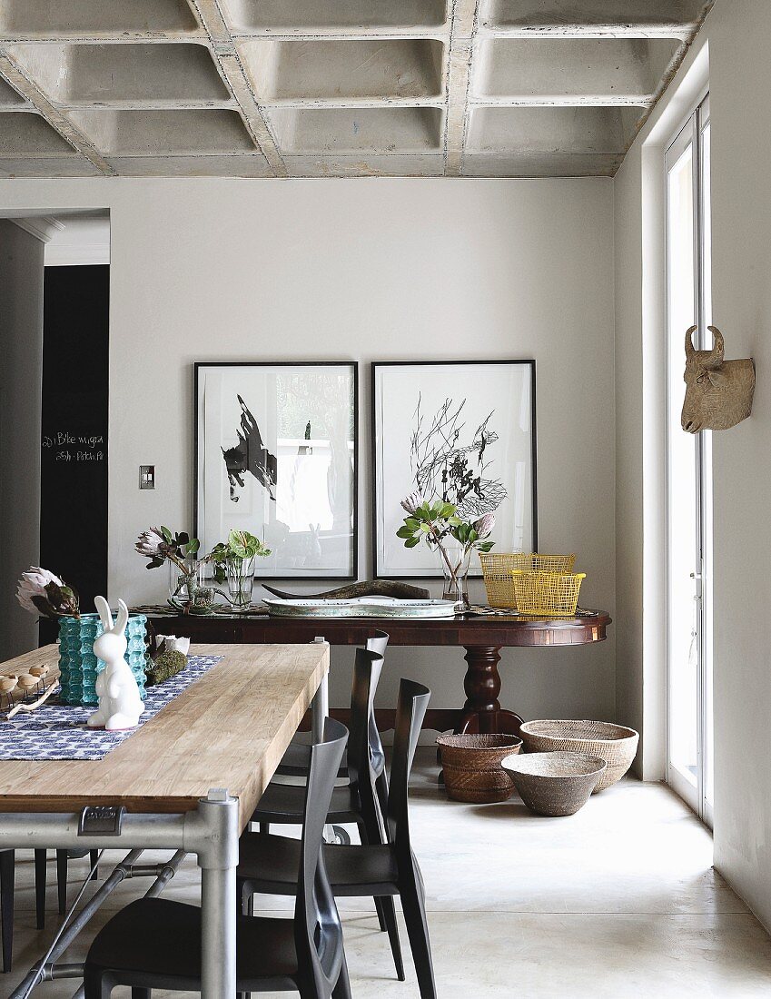 Contemporary table, dark chairs and antique console table in dining room with concrete coffered ceiling