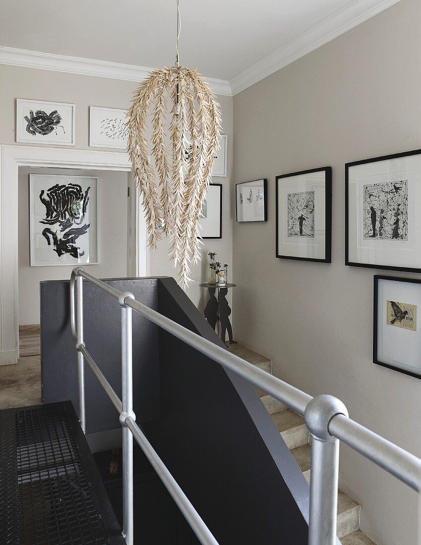 Designer pendant lamp and gallery of artworks in stairwell with metal landing balustrade and black, masonry stair balustrade