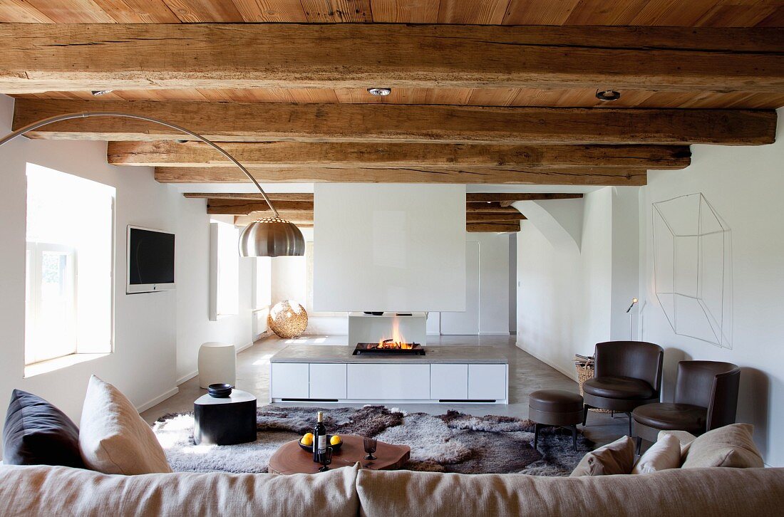 Loungebereich mit weißem Gaskamin, Kaminfeuer und sichtbaren rustikalen Balken