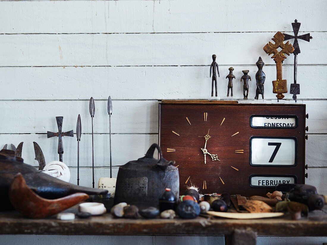 Stillleben aus Reisemitbringsel, verschiedene Figuren aus Metall auf alter Uhr vor weisser, holzverschalter Wand