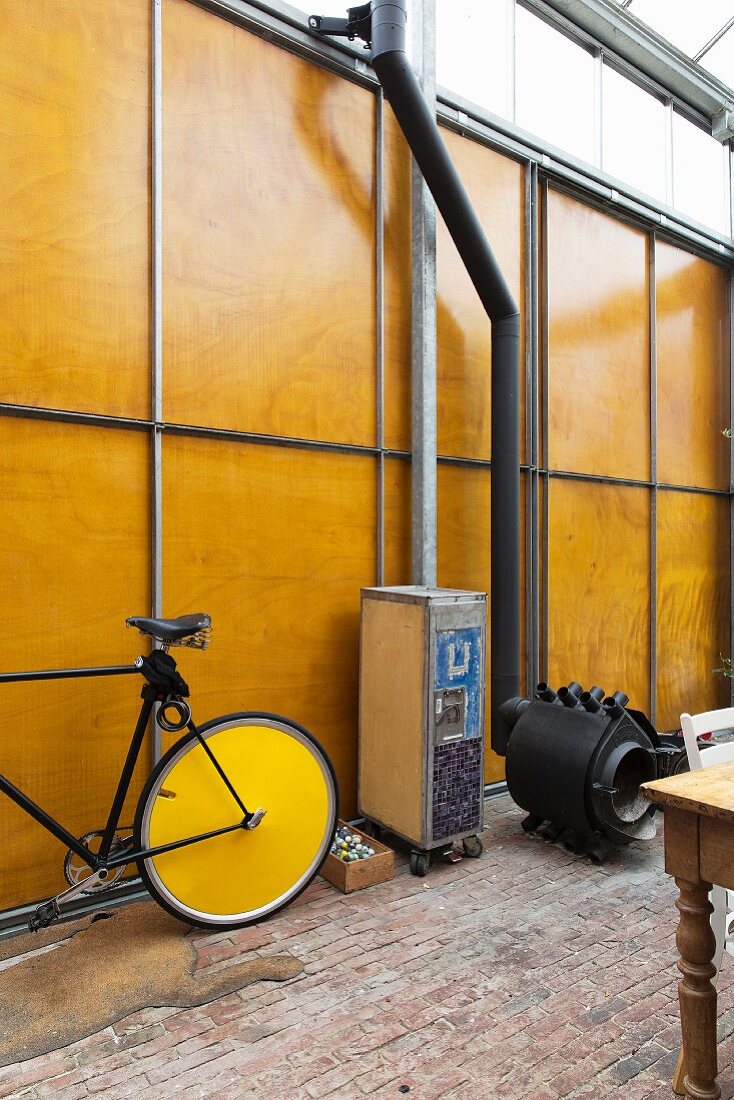 Herrenrad und Rollcontainer neben schwarzem Bullerjan Ofen vor hoher Holz-Metallwand