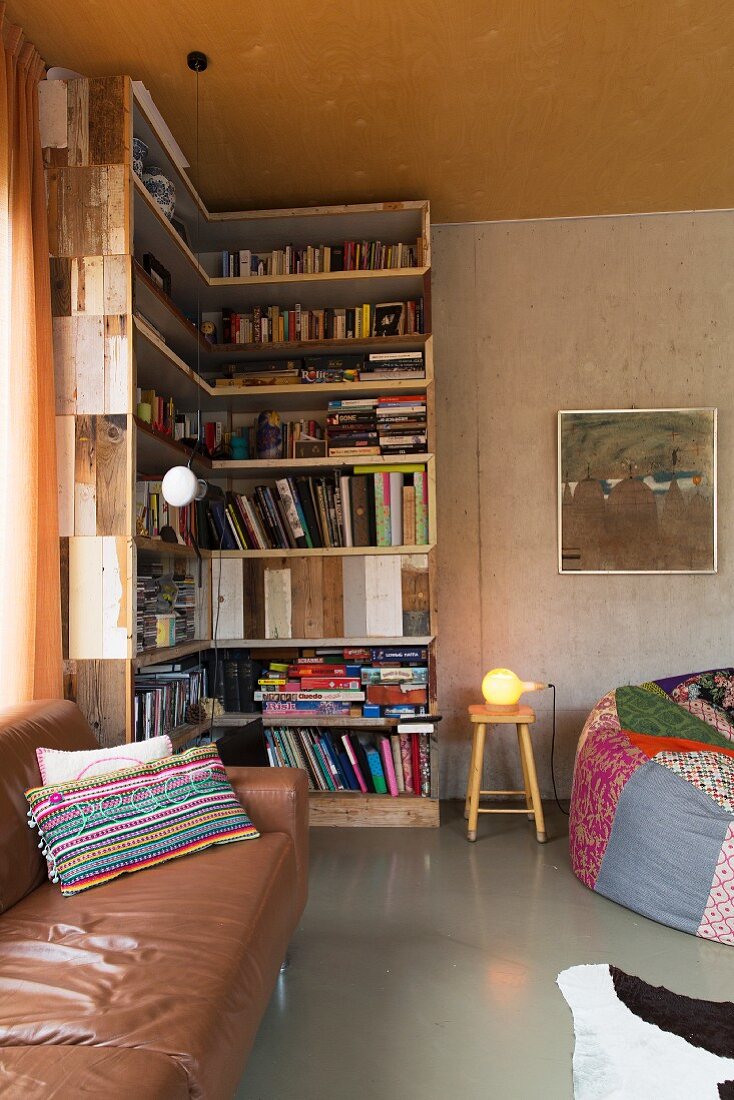 Ledercouch vor Übereck-Bücherregal aus wiederverwendeten Brettern in Wohnraumecke mit Patchwork-Sitzsack