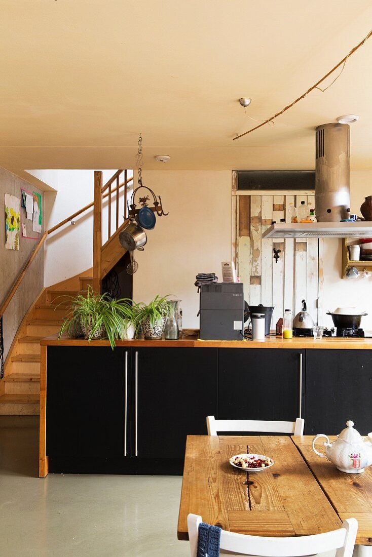 Essplatz vor Küchenzeile mit Holzrahmen um schwarze Unterschränke und seitlich gewendelter Treppenaufgang