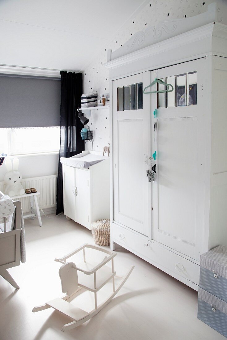Kinderzimmer mit weiß lackierten Retro- und Vintagemöbeln, dazu grauer Rollo, schwarzer Vorhang und Sternenmotiv-Tapete
