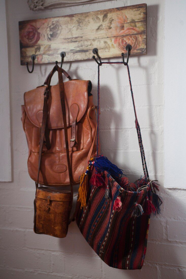 Verschiedene Taschen hängen an Vintage-Holzgarderobe mit Rosenmotiv