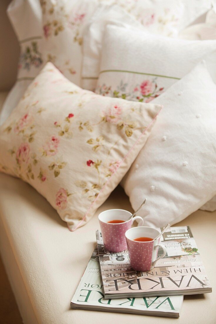 Magazines and teacups on bed with romantic floral bed linen