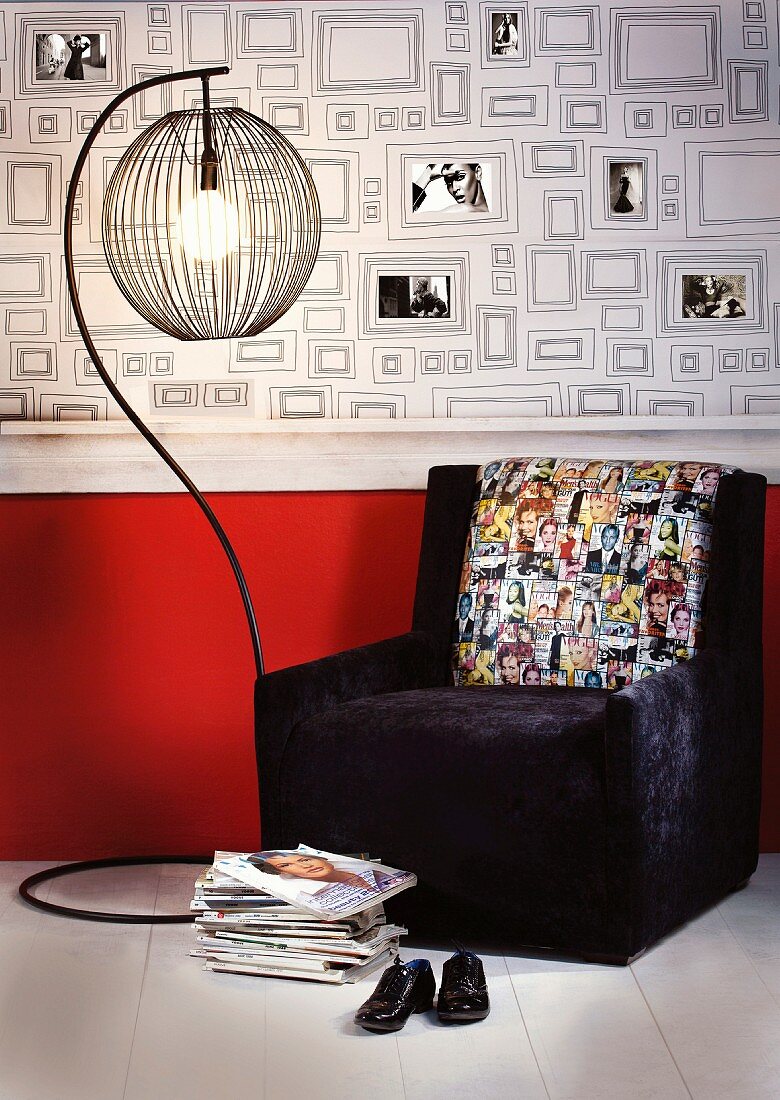 Dark armchair with photo motifs on cushion and standard lamp in front of wallpaper with pattern of picture frames