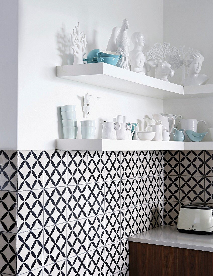 Fliesen mit schwarz-weißem, geometrischem Muster an Wand, oberhalb Regalböden mit Geschirr und Dekofiguren in Weiß