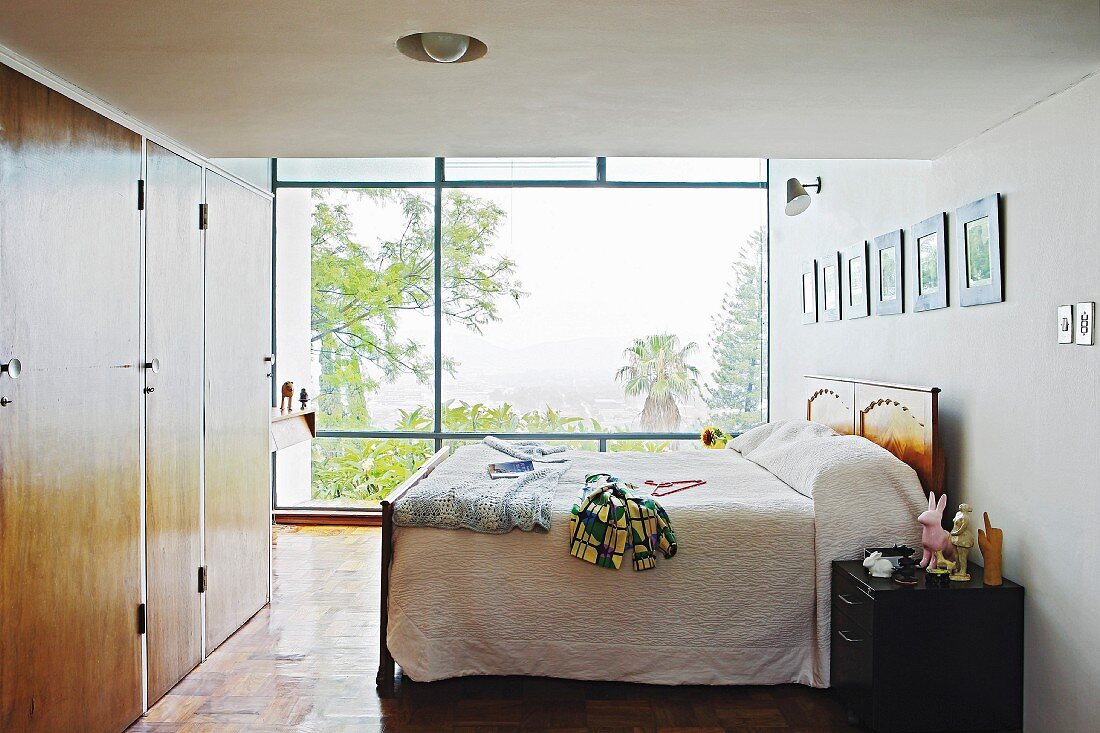 Boxspringbett und Einbauschrank mit Holztüren im Schlafzimmer, im Hintergrund Fensterfront mit Gartenblick