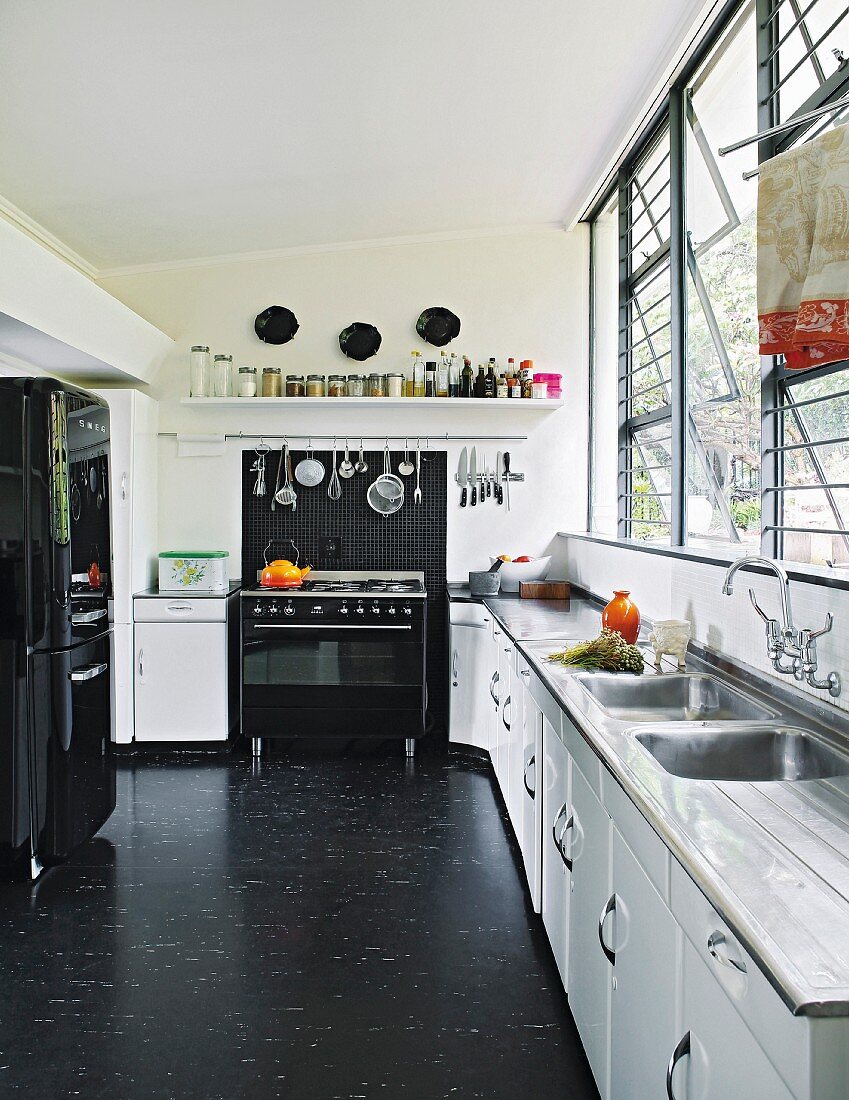 Black and white kitchen with long counter below bank of windows and black vinyl floor