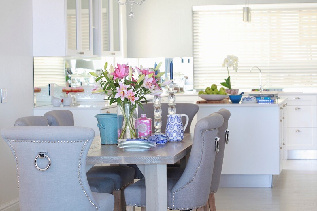 Eleganter Essplatz mit edlen Polsterstühlen, Lilien und Geschirr auf dem Tisch in offener Küche