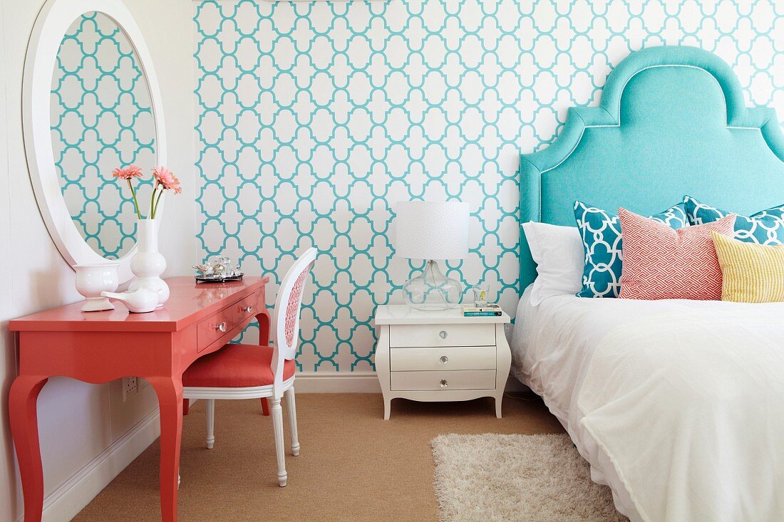 Bed with turquoise headboard and salmon-pink dressing table in bedroom