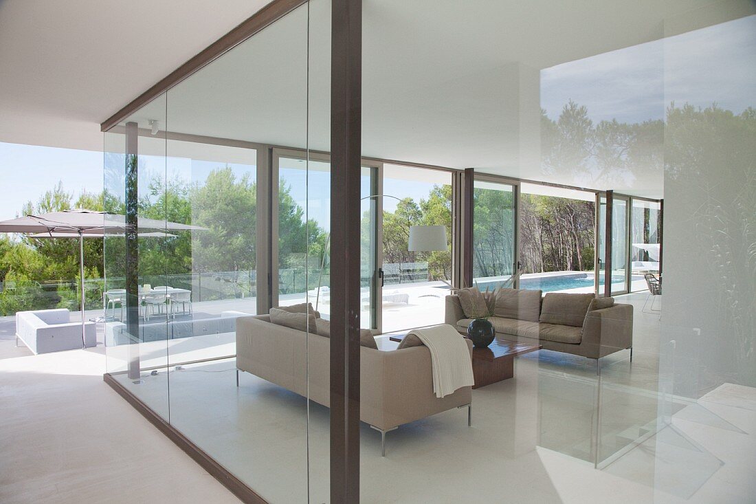 Blick durch raumhohe Glasfront auf eleganten Wohnbereich und auf Terrasse mit Pool