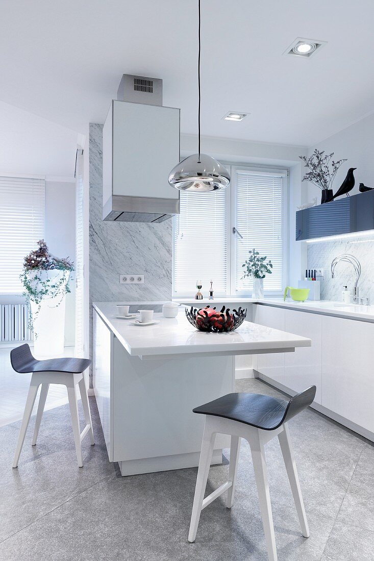 White kitchen counter with protruding table and bar stools in open-plan designer kitchen