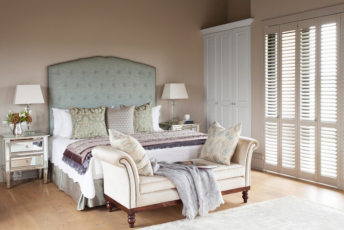 Schlafzimmer in elegantem Landhausstil mit antiker Bettbank vor Doppelbett mit hohem Kopfteil