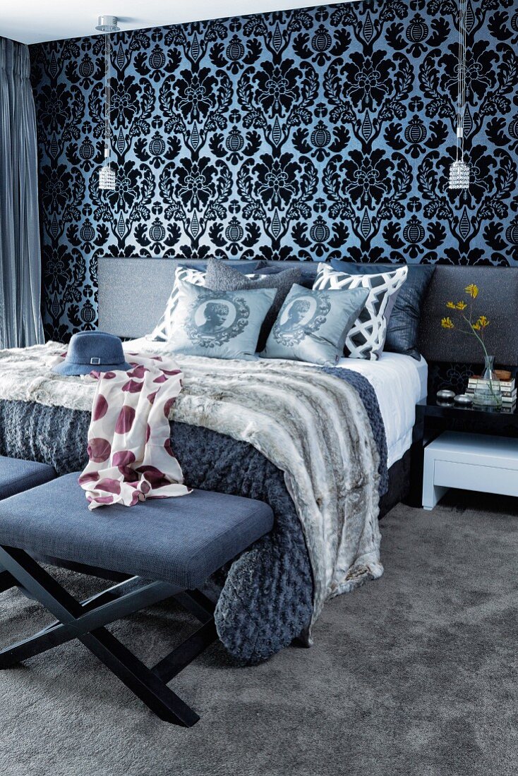 Ornate wallpaper and scatter cushions on double bed in bedroom with dark colour scheme