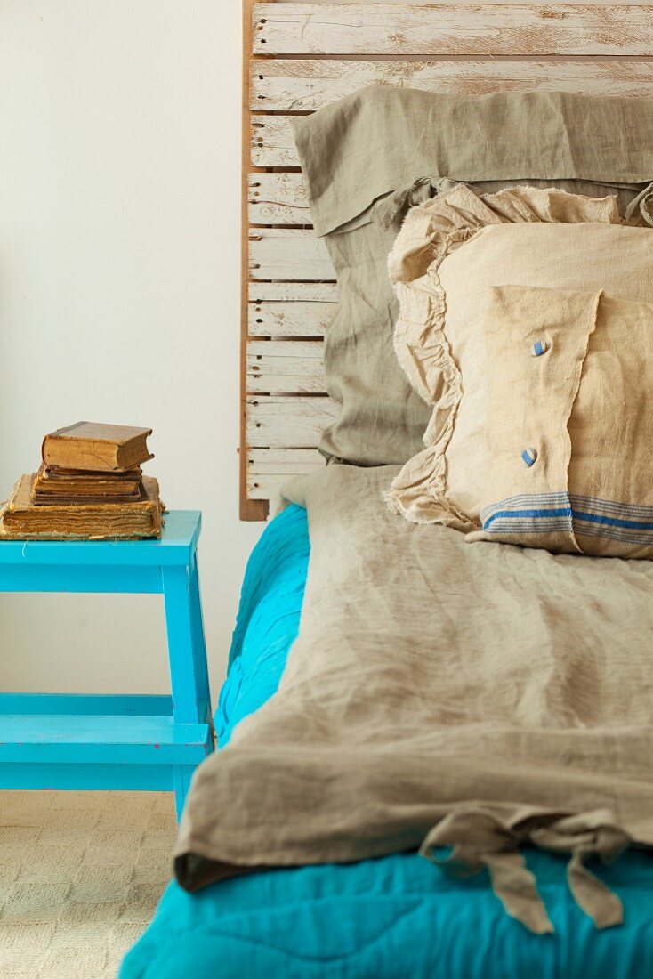 Selbstgebautes Bett mit rustikalem Kopfende aus Holz und rustikaler Leinenbettwäsche