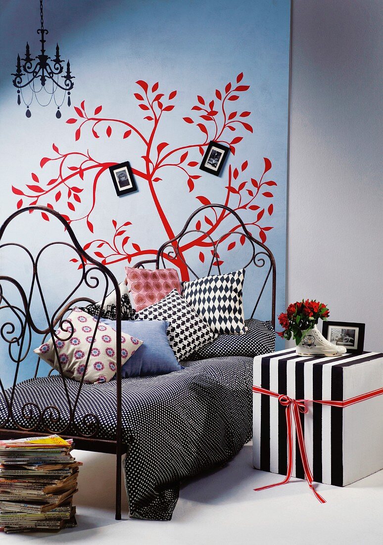 Black and white striped cubic side table next to metal bed against poster of red, stylised tree on wall