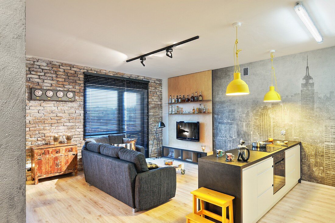 Küchentheke und Polstersofa in offenem Wohnraum mit Backsteinwand und Fototapete