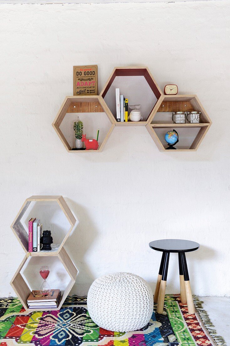 Hexagonal wooden shelving units on wall and on floor next to pouffe and stool