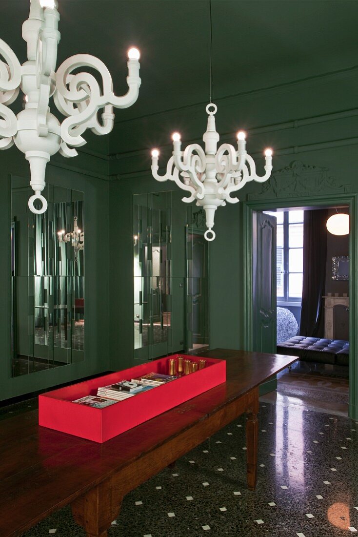 Modern white chandeliers in dark green room with coffered walls and terazzo floor