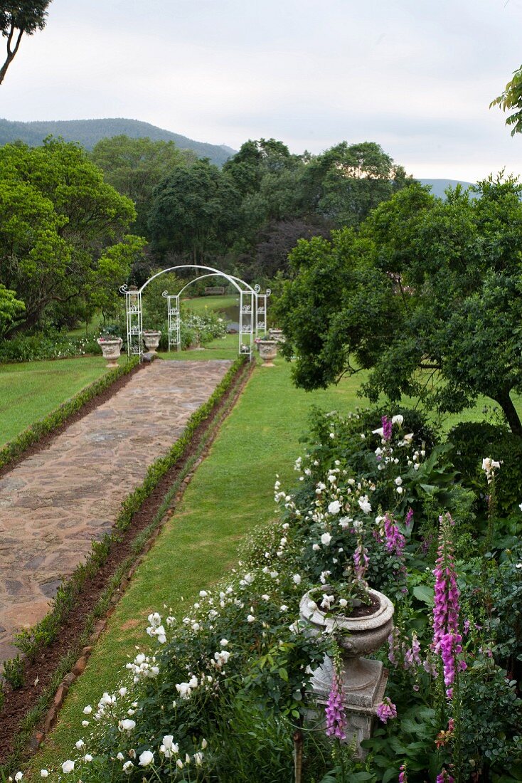 Stone-paved path leading to white trellis arch in large garden
