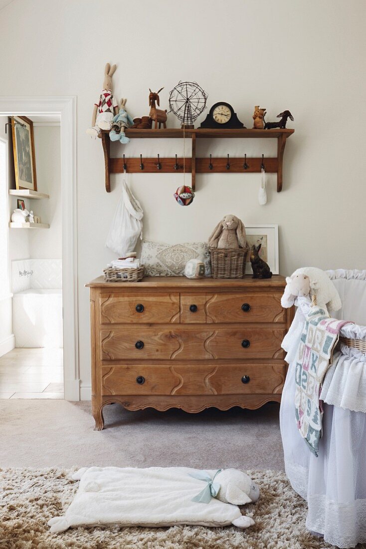 Traditional bassinet, chest of drawers and vintage shelves with hooks in nursery