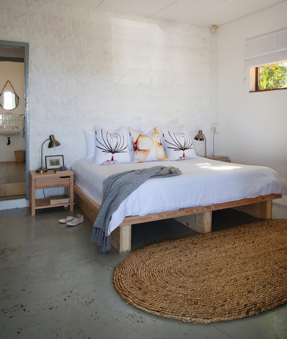 Doppelbett mit Holzuntergestell und ovaler Sisalteppich in schlichtem Schlafzimmer