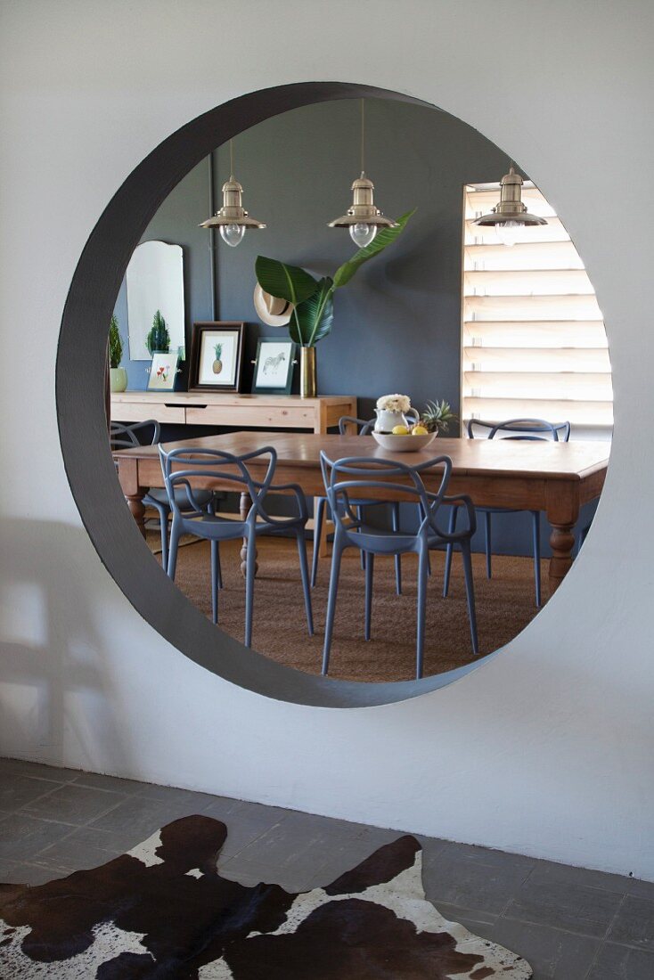 View of dining table and chairs seen through round aperture in wall