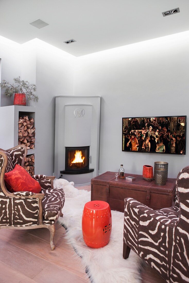 Zebra-print armchairs and orange, drum-shaped side table in room with corner fireplace and suspended ceiling