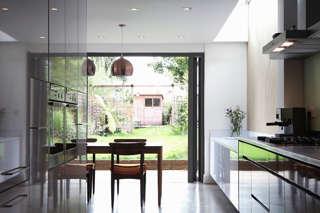 Open-plan kitchen with glossy cabinets and dining area in front of folding terrace doors