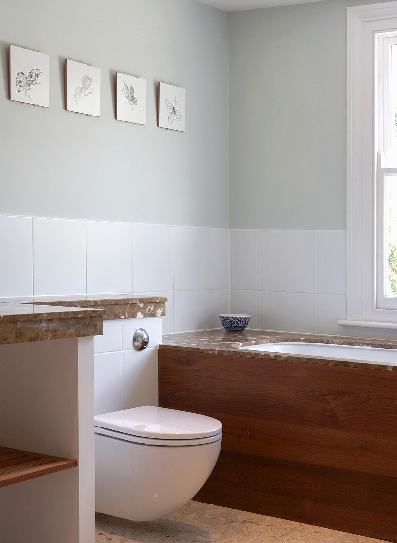 Toilet and built-in bathtub against wall with half-height white tiles