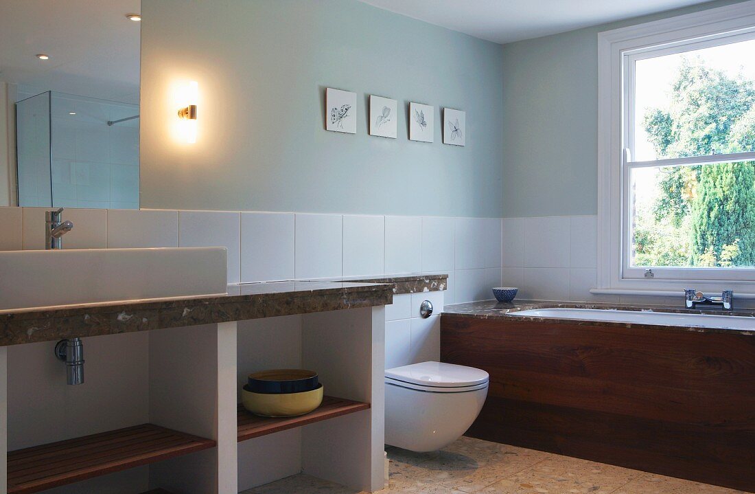 Washstand and toilet against wall with half-height white tiles and fitted bathtub below window