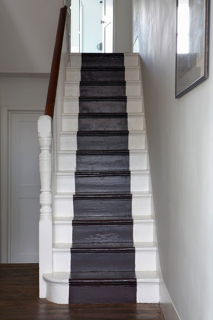 Stairwell with black, runner-style stripe down centre of white, wooden stairs