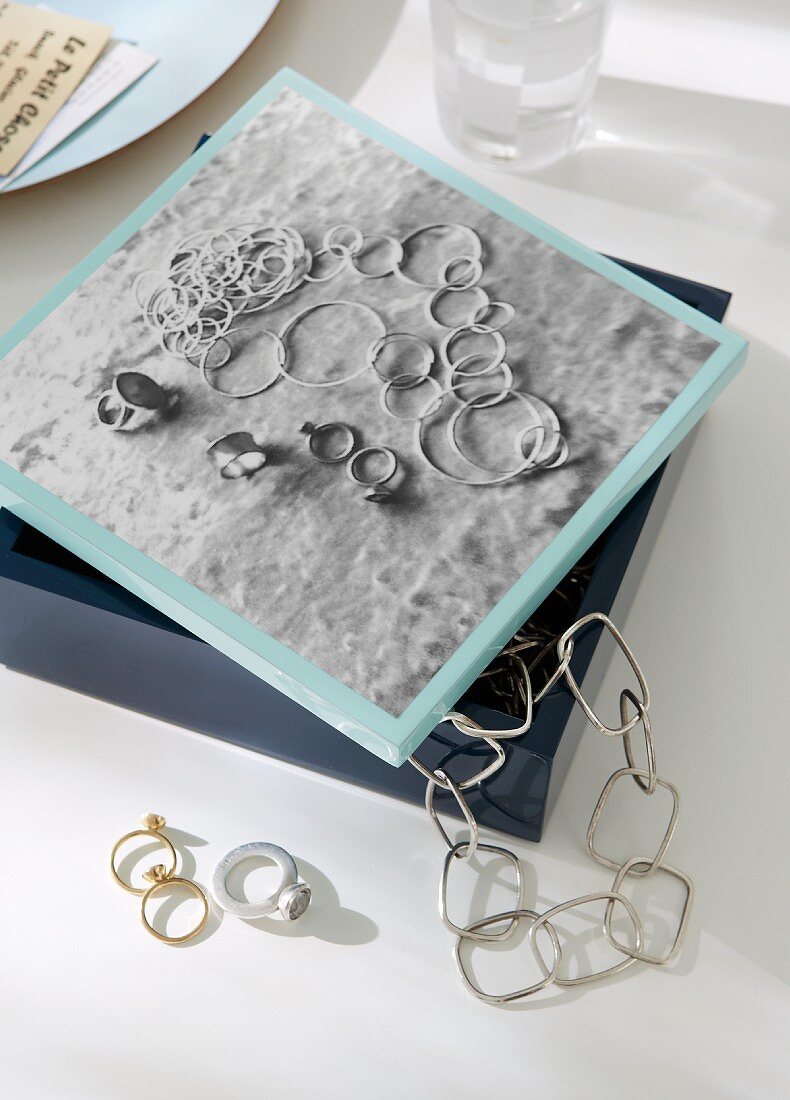 Black and white photo of chains and rings on silver-grey velvet decorating lid of jewellery box