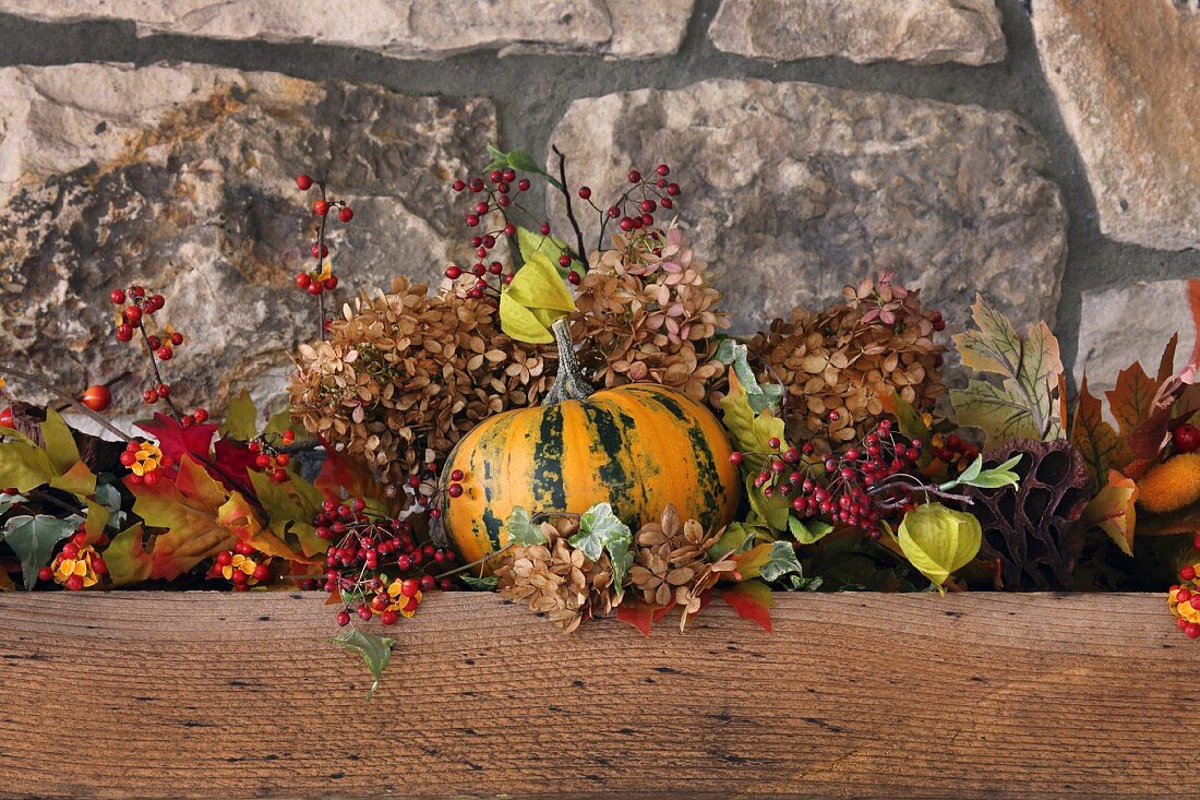 Herbstliche Deko mit Kürbis, Beerenzweigen und Blättern, vor Natursteinwand