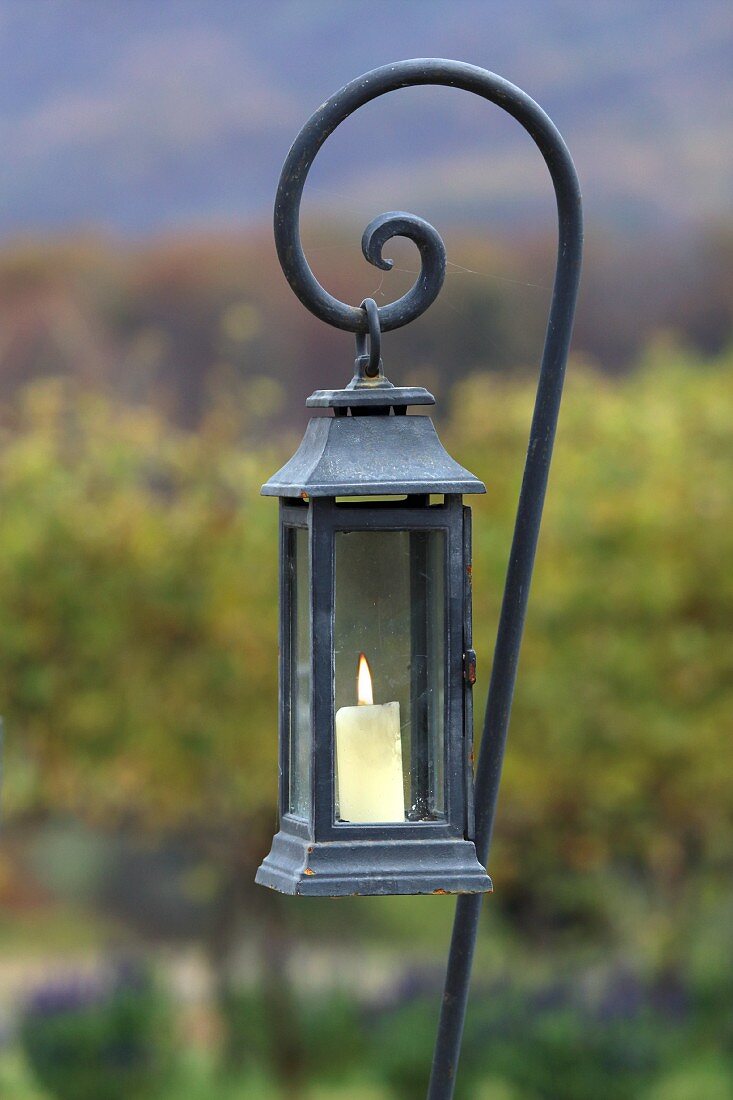 Lit candle in lantern hanging from iron rod with spiral ens
